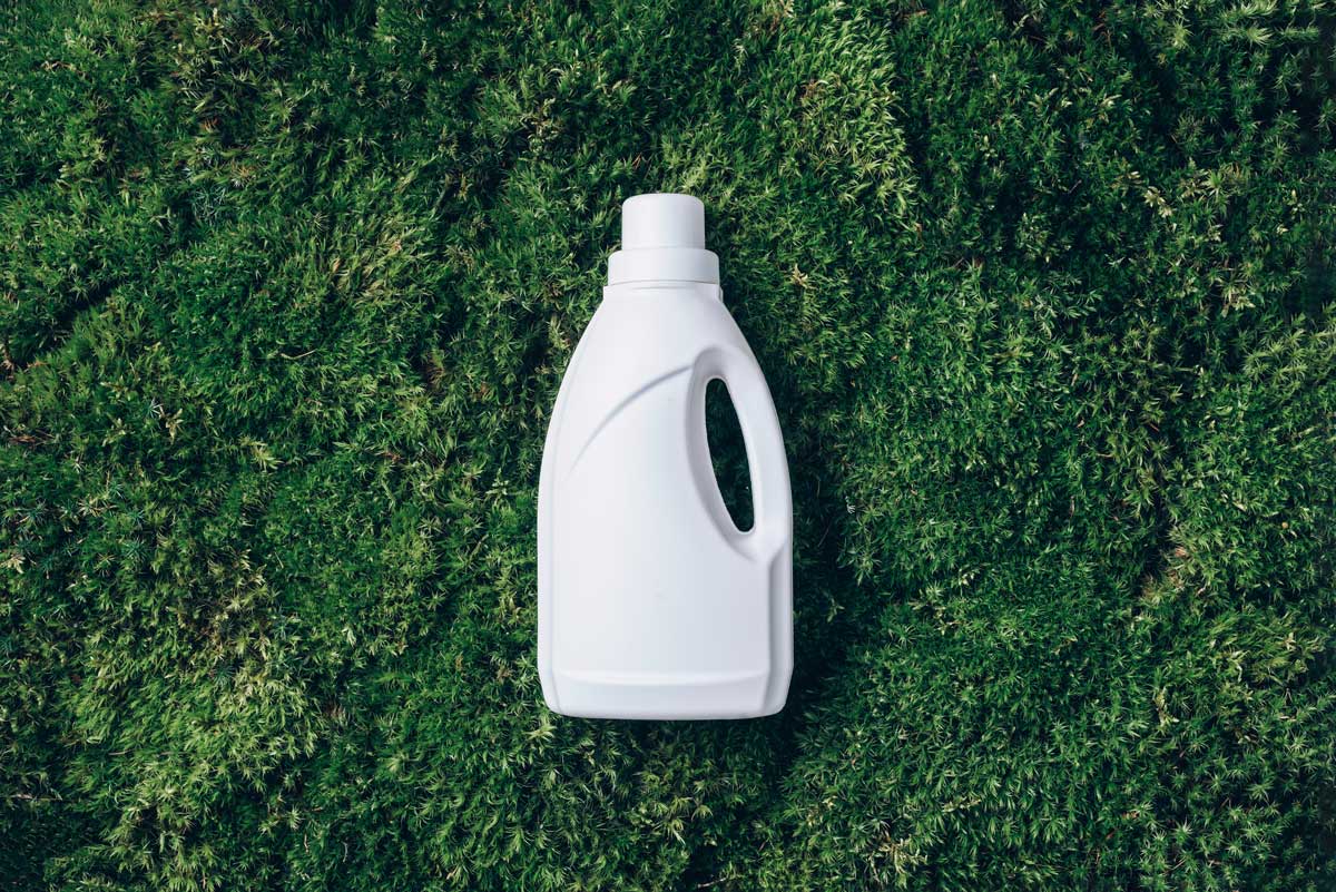 White plastic bottle of cleaning product, household chemicals or liquid laundry detergent on green grass, moss background. Top view. Flat lay.