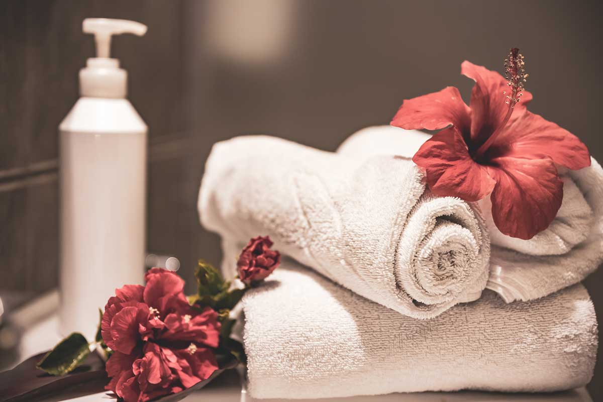 Spa composition with rolled clean towels, fresh flowers and a care product in a bottle with a dispenser in the bathroom.
