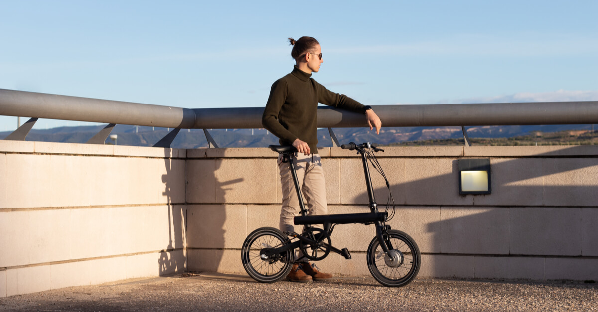 Young man using a folding electric bicycle to move in the city where he lives and be greener with the environment ways to reduce carbon footprint